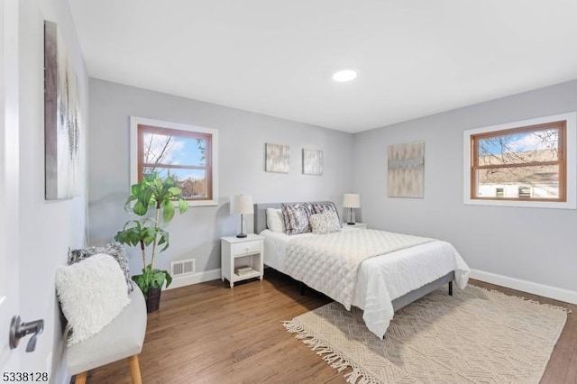 bedroom with baseboards, multiple windows, visible vents, and wood finished floors