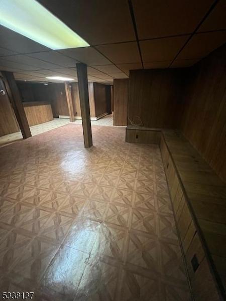 basement with a drop ceiling, wood walls, and light parquet floors