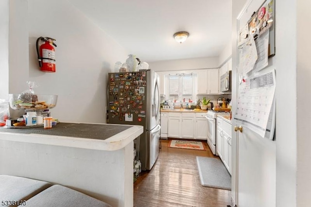 kitchen with white cabinetry, kitchen peninsula, dark hardwood / wood-style flooring, appliances with stainless steel finishes, and a breakfast bar area