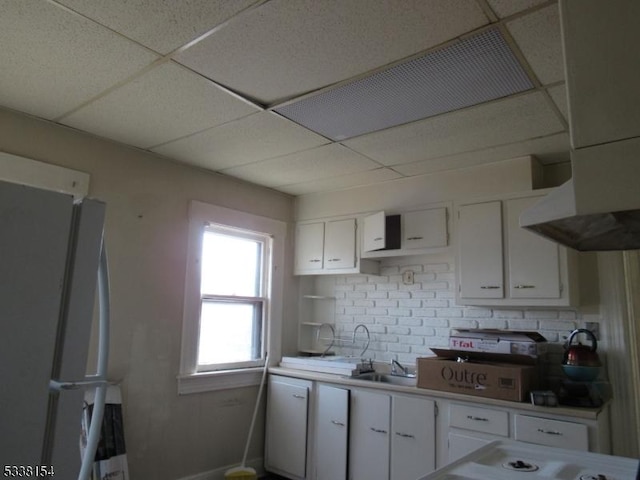 kitchen featuring white cabinetry, sink, white fridge, and a drop ceiling