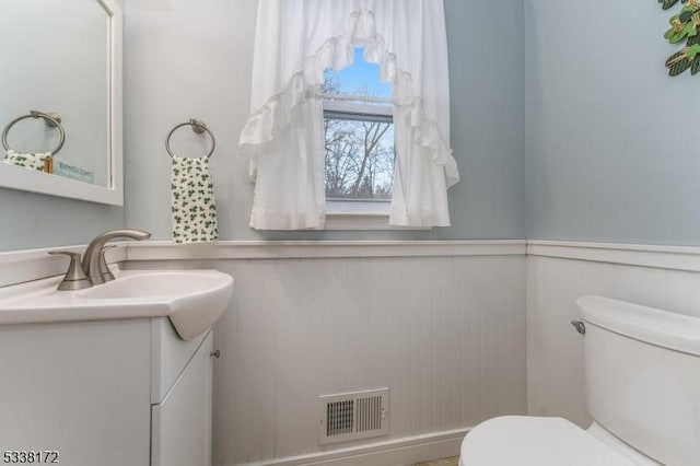 half bath featuring a wainscoted wall, visible vents, vanity, and toilet