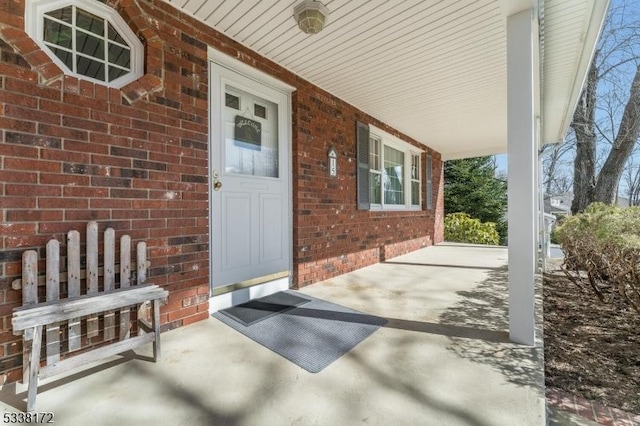 view of exterior entry featuring a porch and brick siding