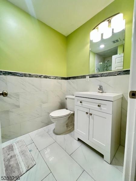 bathroom featuring vanity, tile walls, and toilet