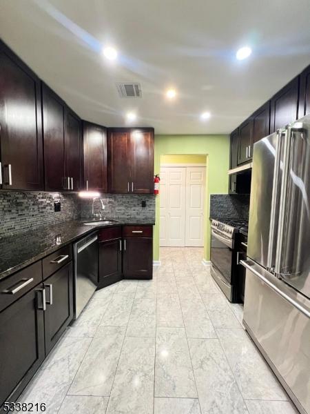 kitchen with appliances with stainless steel finishes, sink, dark stone countertops, and decorative backsplash