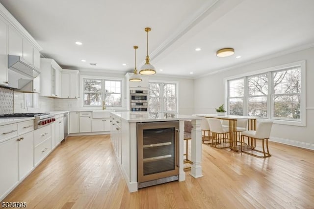 kitchen featuring hanging light fixtures, stainless steel appliances, white cabinets, a kitchen island, and beverage cooler