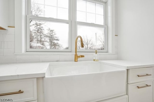 details featuring white cabinetry, sink, decorative backsplash, and light stone countertops