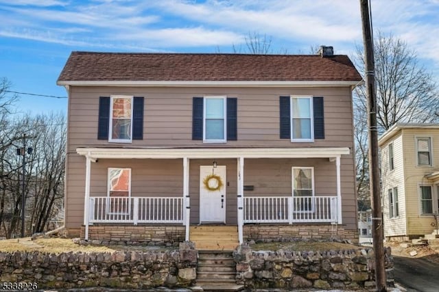 view of front of home with covered porch, roof with shingles, and a chimney