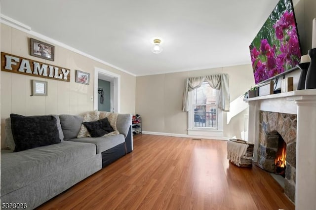 living area featuring crown molding, a stone fireplace, baseboards, and wood finished floors