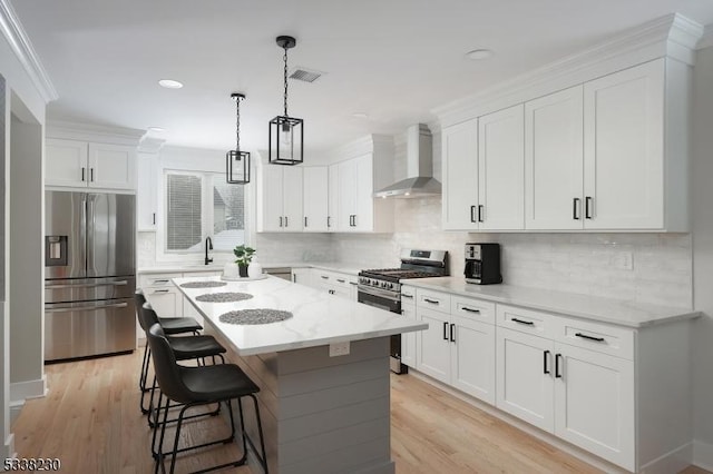 kitchen with wall chimney exhaust hood, light stone counters, a center island, stainless steel appliances, and white cabinets