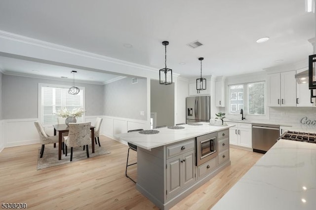 kitchen featuring pendant lighting, white cabinetry, stainless steel appliances, a center island, and light stone counters