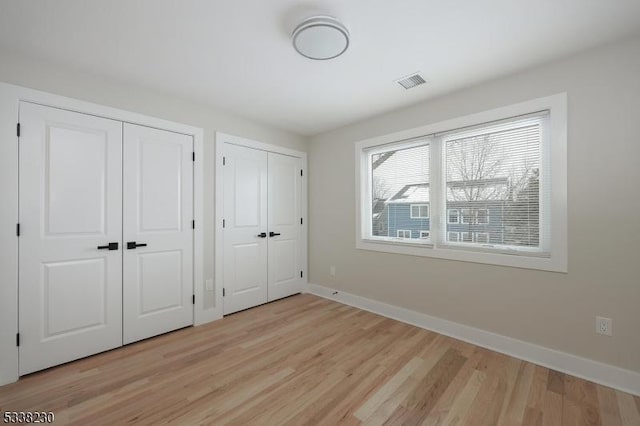 unfurnished bedroom with two closets and light wood-type flooring