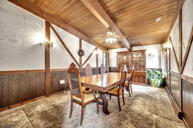 dining area featuring wooden walls, beam ceiling, light colored carpet, and wooden ceiling