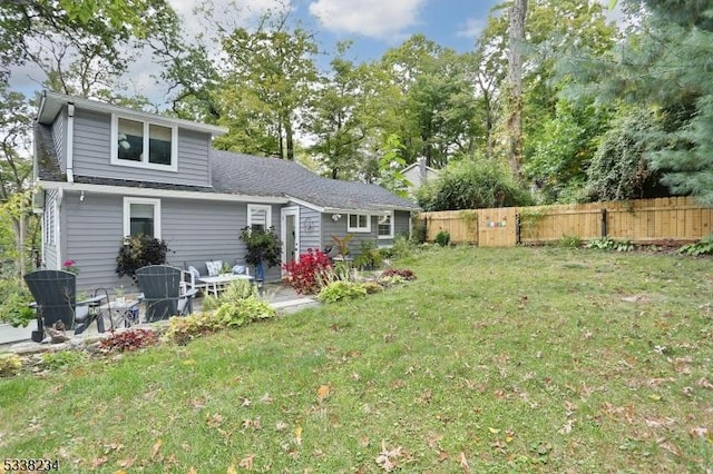 back of property with roof with shingles, fence, and a lawn