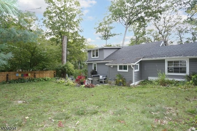 rear view of house featuring a shingled roof, fence, and a lawn