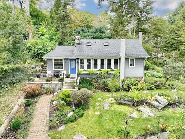 view of front of house featuring a chimney, a front lawn, and roof with shingles