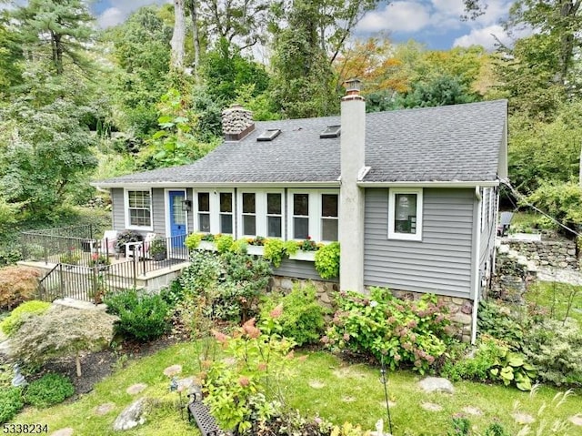 back of property with roof with shingles, a chimney, and fence