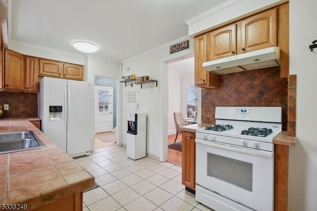 kitchen with backsplash, tile counters, under cabinet range hood, light tile patterned flooring, and white appliances