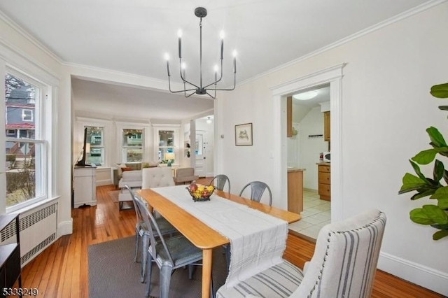 dining space with an inviting chandelier, crown molding, radiator heating unit, and light wood-style floors