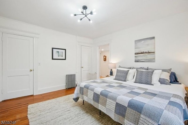 bedroom with an inviting chandelier, radiator, wood finished floors, and baseboards