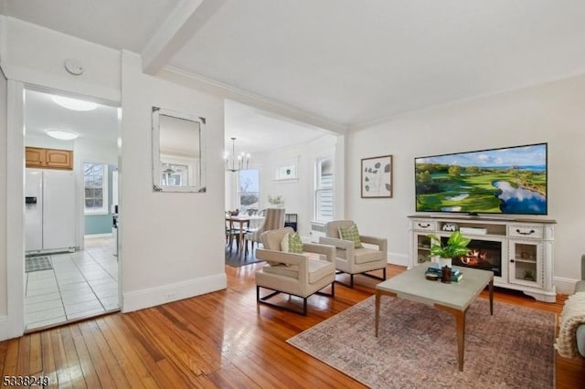 living room featuring a chandelier, beam ceiling, light wood-type flooring, and baseboards