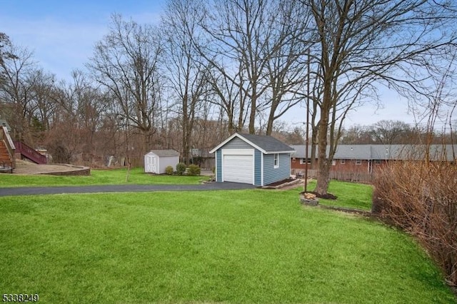 view of yard featuring a storage unit, an outbuilding, driveway, a detached garage, and fence