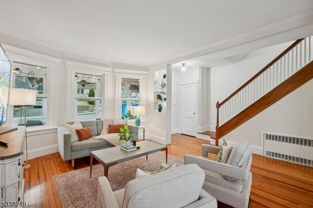 living area with stairway, baseboards, light wood-style flooring, and radiator heating unit