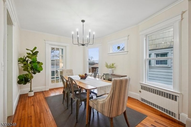 dining area featuring wood finished floors, baseboards, an inviting chandelier, radiator heating unit, and crown molding