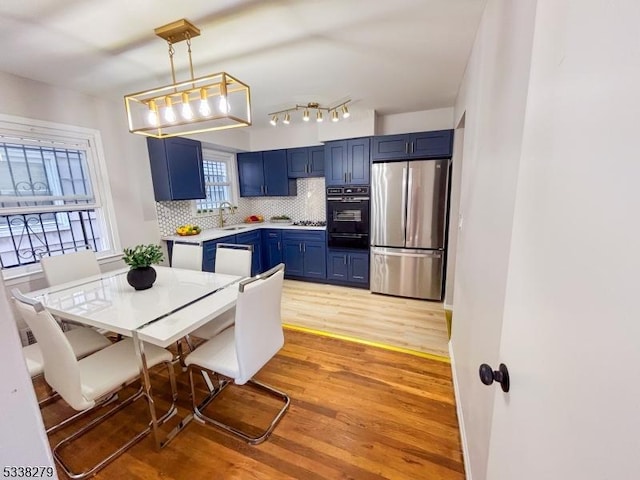 kitchen featuring light wood-style flooring, freestanding refrigerator, decorative backsplash, light countertops, and blue cabinets