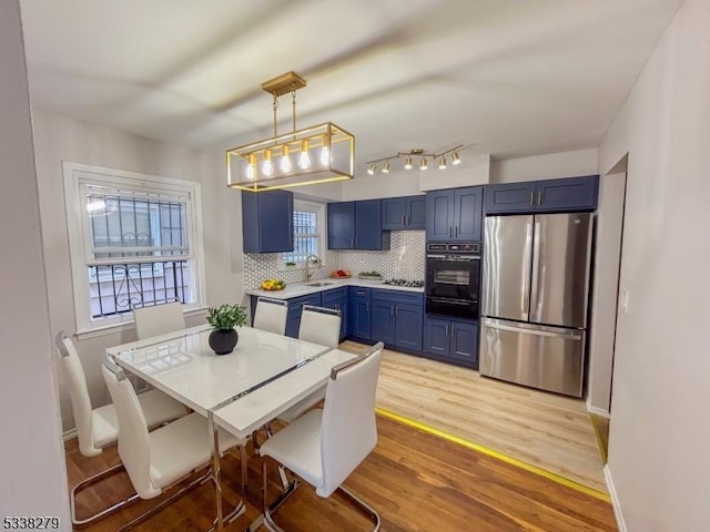 kitchen featuring oven, blue cabinetry, freestanding refrigerator, light wood finished floors, and light countertops