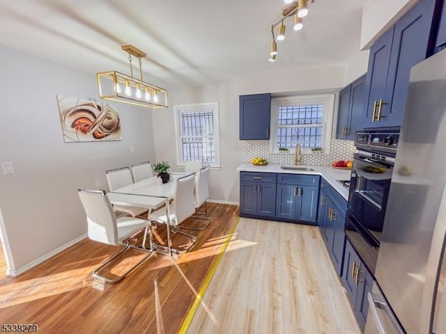 kitchen featuring blue cabinetry, black oven, a sink, light countertops, and decorative backsplash