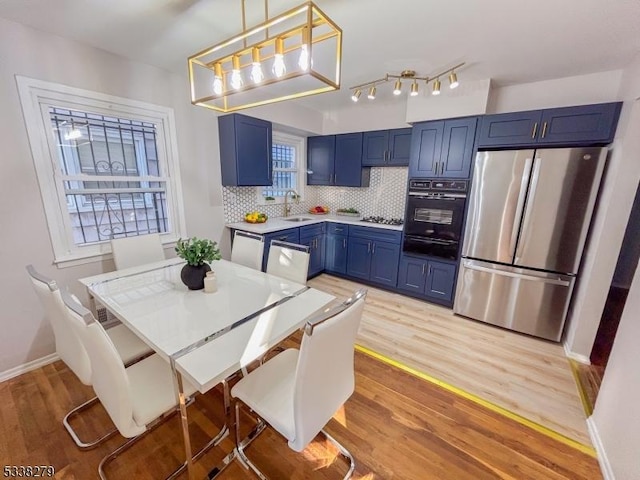 kitchen featuring light wood-type flooring, blue cabinetry, a sink, stainless steel appliances, and tasteful backsplash