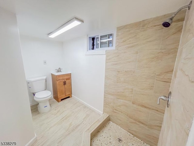 bathroom featuring toilet, tiled shower, vanity, and baseboards