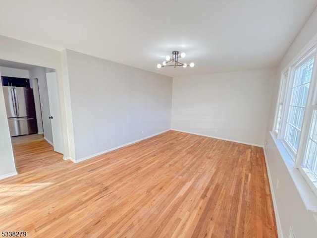 unfurnished room featuring baseboards, light wood-style floors, and an inviting chandelier