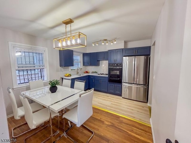 kitchen featuring backsplash, light wood-type flooring, light countertops, appliances with stainless steel finishes, and blue cabinets