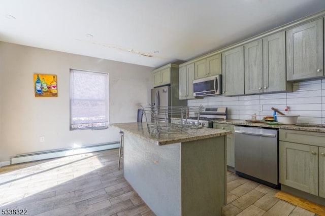 kitchen featuring dark stone counters, baseboard heating, a kitchen island, stainless steel appliances, and backsplash