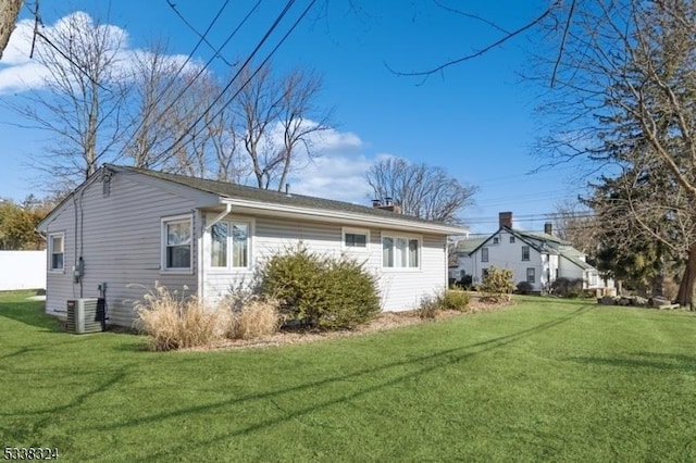 view of side of property with cooling unit, a lawn, and a chimney