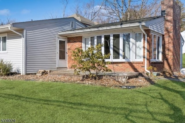 exterior space featuring brick siding, a yard, and a chimney