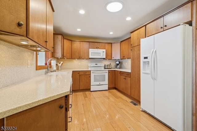 kitchen featuring light countertops, light wood-style floors, brown cabinetry, a sink, and white appliances