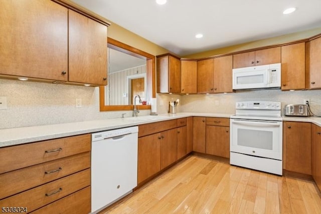 kitchen featuring light wood-style flooring, white appliances, a sink, light countertops, and decorative backsplash