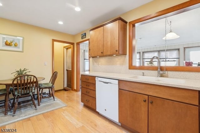 kitchen featuring white dishwasher, a sink, light countertops, light wood-type flooring, and backsplash