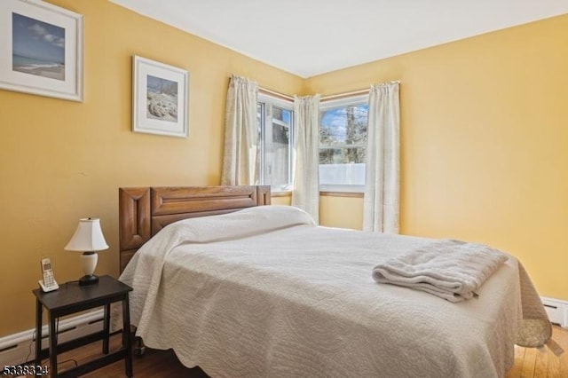 bedroom with a baseboard heating unit, baseboards, and wood finished floors