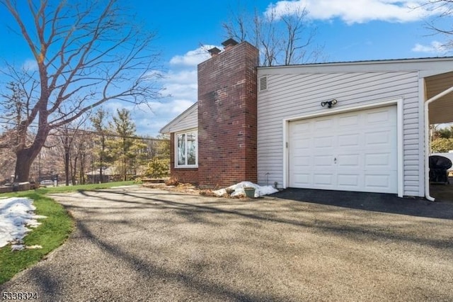 view of property exterior featuring a garage, a chimney, and aphalt driveway