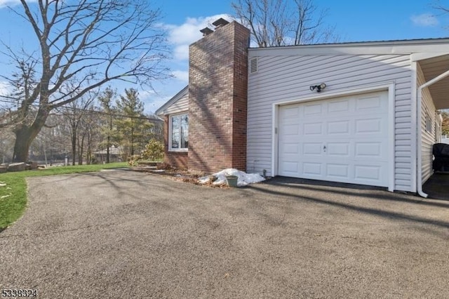 view of side of home with a garage, a chimney, and aphalt driveway