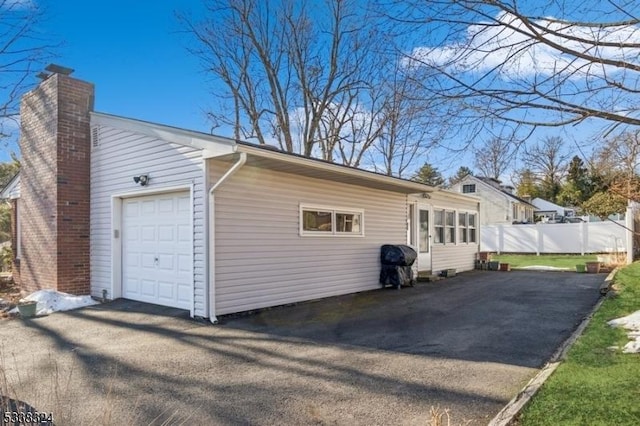 view of property exterior with a garage, a chimney, fence, and aphalt driveway