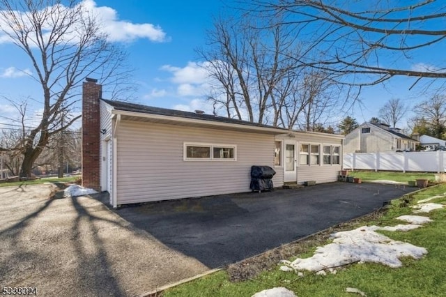 rear view of house featuring aphalt driveway, fence, and a chimney