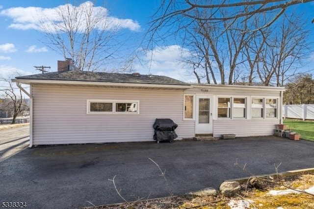 back of property featuring a chimney, fence, aphalt driveway, and a patio