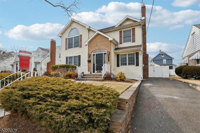 traditional-style home with aphalt driveway, a detached garage, fence, a gate, and a chimney