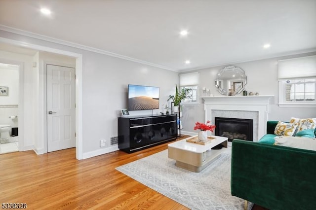 living room featuring ornamental molding, light wood finished floors, plenty of natural light, and a glass covered fireplace