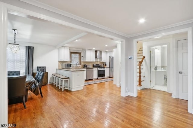 kitchen featuring stainless steel appliances, white cabinets, a sink, wall chimney range hood, and light wood-type flooring