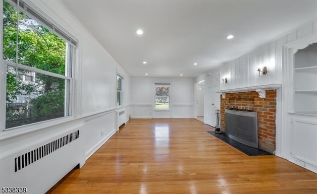 unfurnished living room with crown molding, light wood-type flooring, radiator, built in features, and a fireplace